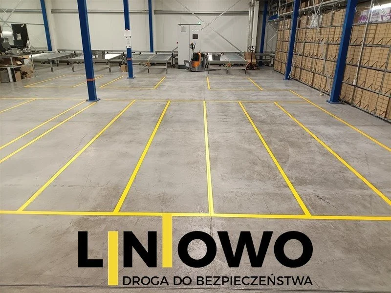 Rząd pól paletowych wyznaczonych żółtymi liniami na posadzce hali magazynowej